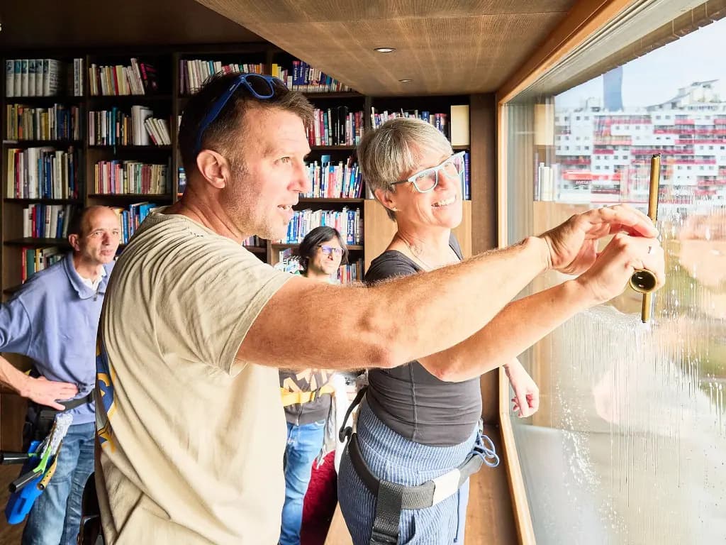 Justin guiding a trainee's squeegee stroke on a window while other trainees watch